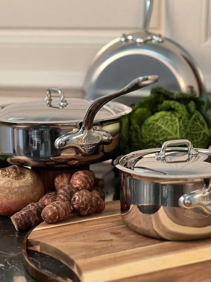 Mauviel M'COOK 5-ply stainless steel sauté pan with lid and cast stainless steel handle, shown in a lifestyle kitchen setting.