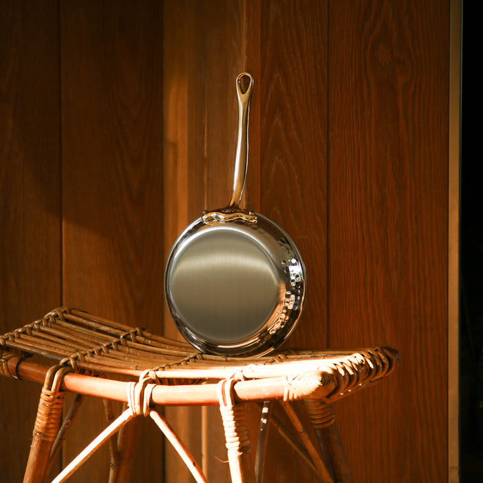 Mauviel M'ELITE B hammered 5-ply frying pan set with brass handles, shown in a lifestyle kitchen setting.