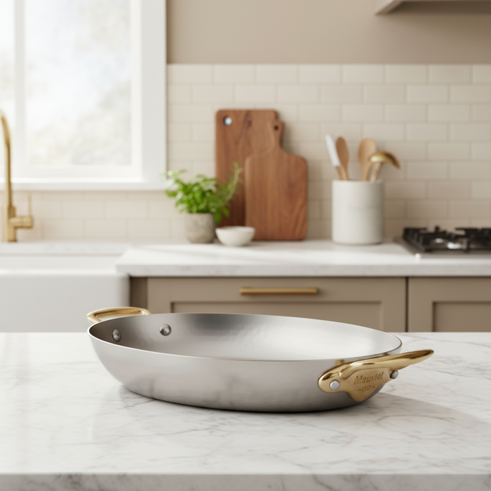 Mauviel M'ELITE B hammered 5-ply oval frying pan with brass handles, showcasing its durable, polished stainless steel surface.