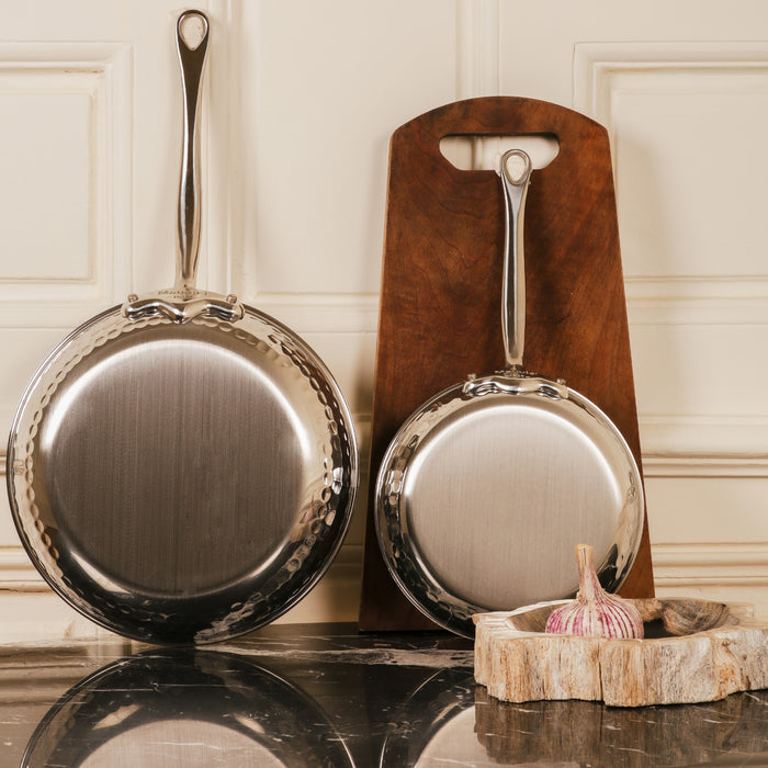 Mauviel M'ELITE hammered 5-ply stainless steel frying pan with cast stainless steel handles, showing a polished, durable cooking surface.